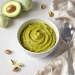 Purée pistache et avocat dans un petit bol, entourée de pistaches et d’avocat frais.